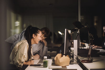 Happy businesswoman discussing with female colleague at desk in office