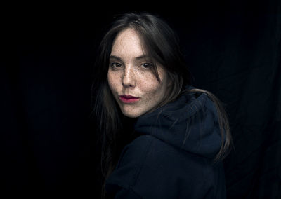 Portrait of woman with freckles against black background