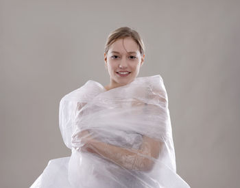 Portrait of smiling woman wrapped in plastic against gray background