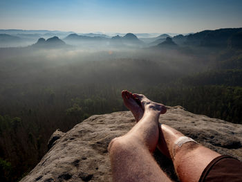 Low section of man relaxing on mountain against sky