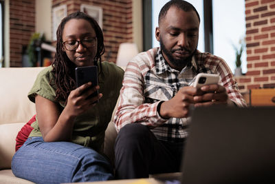 Couple using phone sitting on sofa