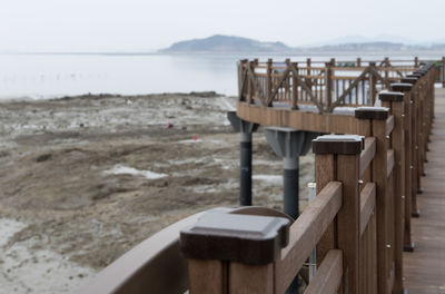 Wooden railing by sea against sky