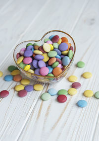 Heartshaped bowl with multicolored dragee sweets on a white wooden background