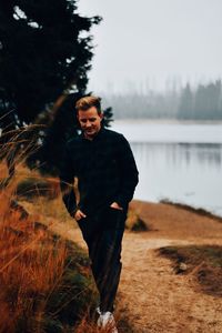 Young man standing by lake against sky