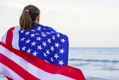 Rear view of woman with flag against sea