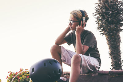 Man holding camera while sitting against clear sky