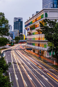 Light trails on city street by buildings against sky