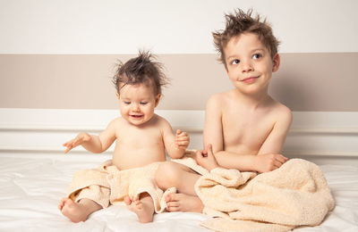 Cute shirtless siblings wrapped in towel against wall