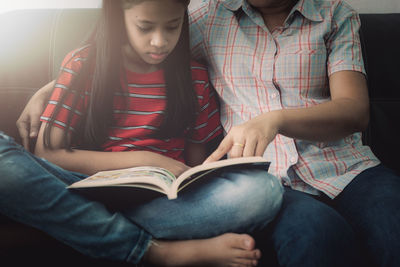 Midsection of woman assisting daughter studying while sitting on sofa at home