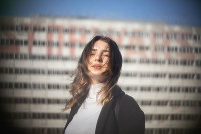 Young woman with eyes closed standing against building in city