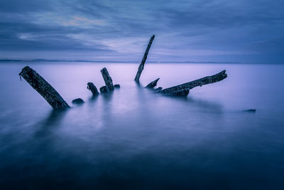 Driftwood in sea against cloudy sky during dusk