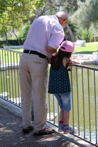 Full length of grandfather and granddaughter standing on bridge