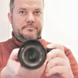 Close-up of man holding dslr camera against white wall