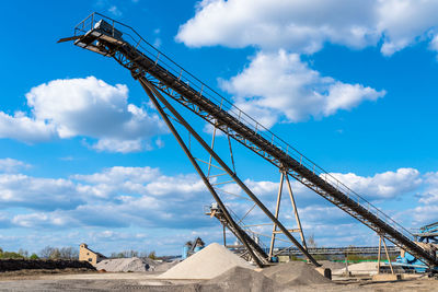 Conveyor over heaps of gravel on blue sky at an industrial cement plant.