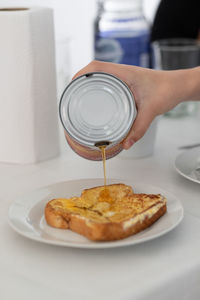 Midsection of person pouring maple syrup on french toast