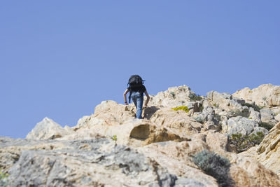 Rear view of man standing on rock against clear blue sky