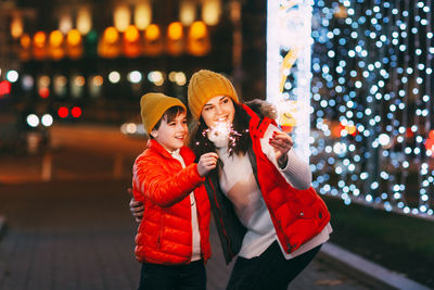 A beautiful boy and his mother celebrate new year or christmas with sparklers on the background 