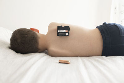 Rear view of shirtless boy with batteries lying on bed