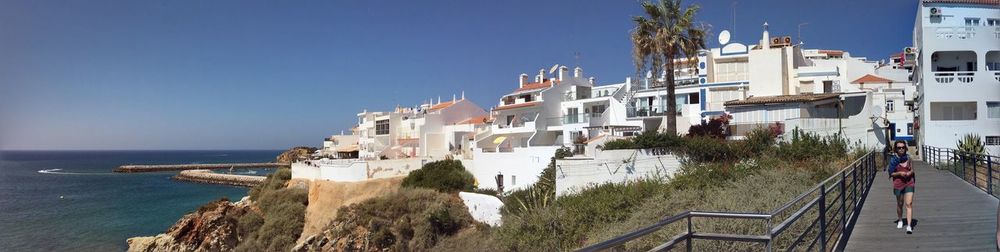 Panoramic shot of woman walking on boardwalk in town by sea