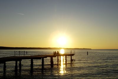 Silhouette pier on sea against clear sky during sunset