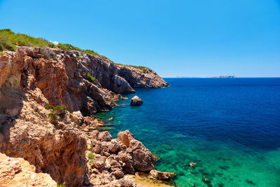 Scenic view of cliff by sea against clear blue sky