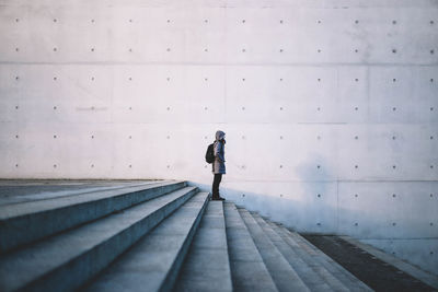 Side view of woman standing on steps against gray wall