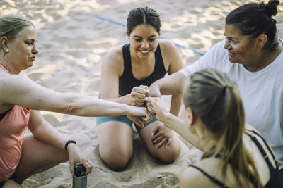 High angle view of female friends giving fist bump while sitting on sand