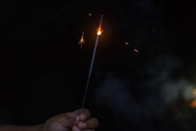 Midsection of person holding sparkler against sky at night