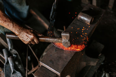 Cropped hand of manual worker hitting on molten metal in factory