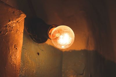 Close-up of illuminated light bulb on wall in darkroom