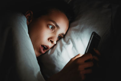 Close-up of woman using phone while lying on bed in darkroom