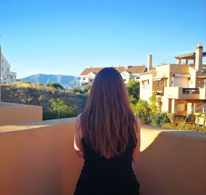 Rear view of woman standing by house against clear sky