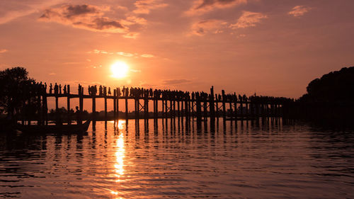 Silhouette wooden posts in sea against sky during sunset