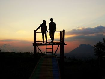 Silhouette couple standing on lookout tower against sky during sunset