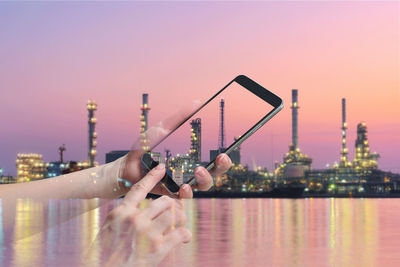 Double exposure image of person using phone and illuminated factory by sea