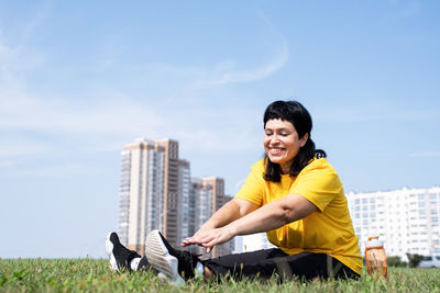 Smiling young man sitting at park against sky