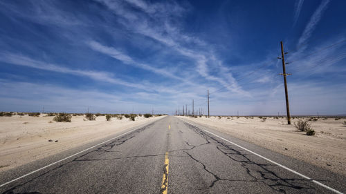 Diminishing perspective of empty road against blue sky during sunny day