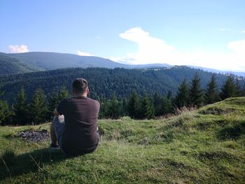 Rear view of man sitting on mountain against sky