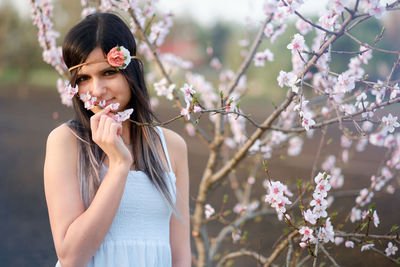 Portrait of young woman standing by cherry tree