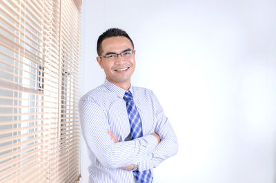 Portrait of smiling businessman with arms crossed standing at office