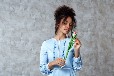 Beautiful woman holding tulip while standing against wall