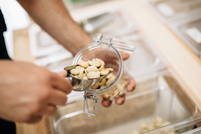 Anonymous female pouring cashews inside glass jar in local store