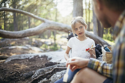 Daughter eating watermelon while looking at father in forest
