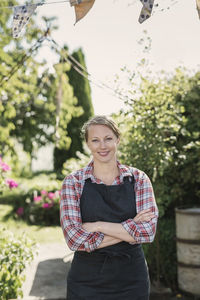 Portrait of smiling woman with crossed arms standing at garden