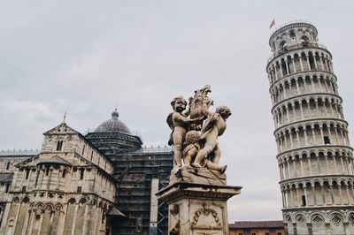 Low angle view of statue and leaning tower of pisa against sky