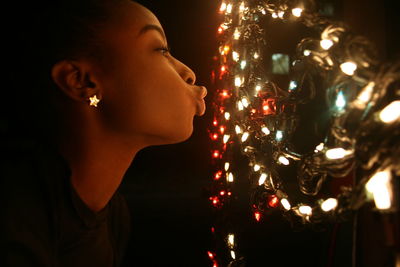 Side view of teenage girl puckering at illuminated string lights