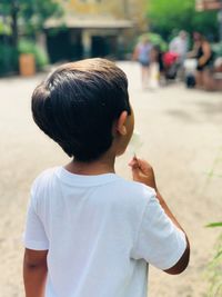 Rear view of boy eating while standing outdoors