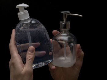 Close-up of hand holding glass bottle against black background