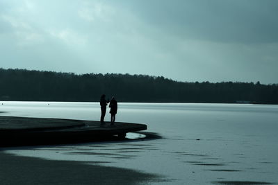 People on lake against sky during winter