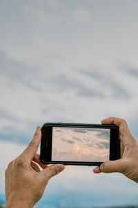 Low section of person using mobile phone against sky